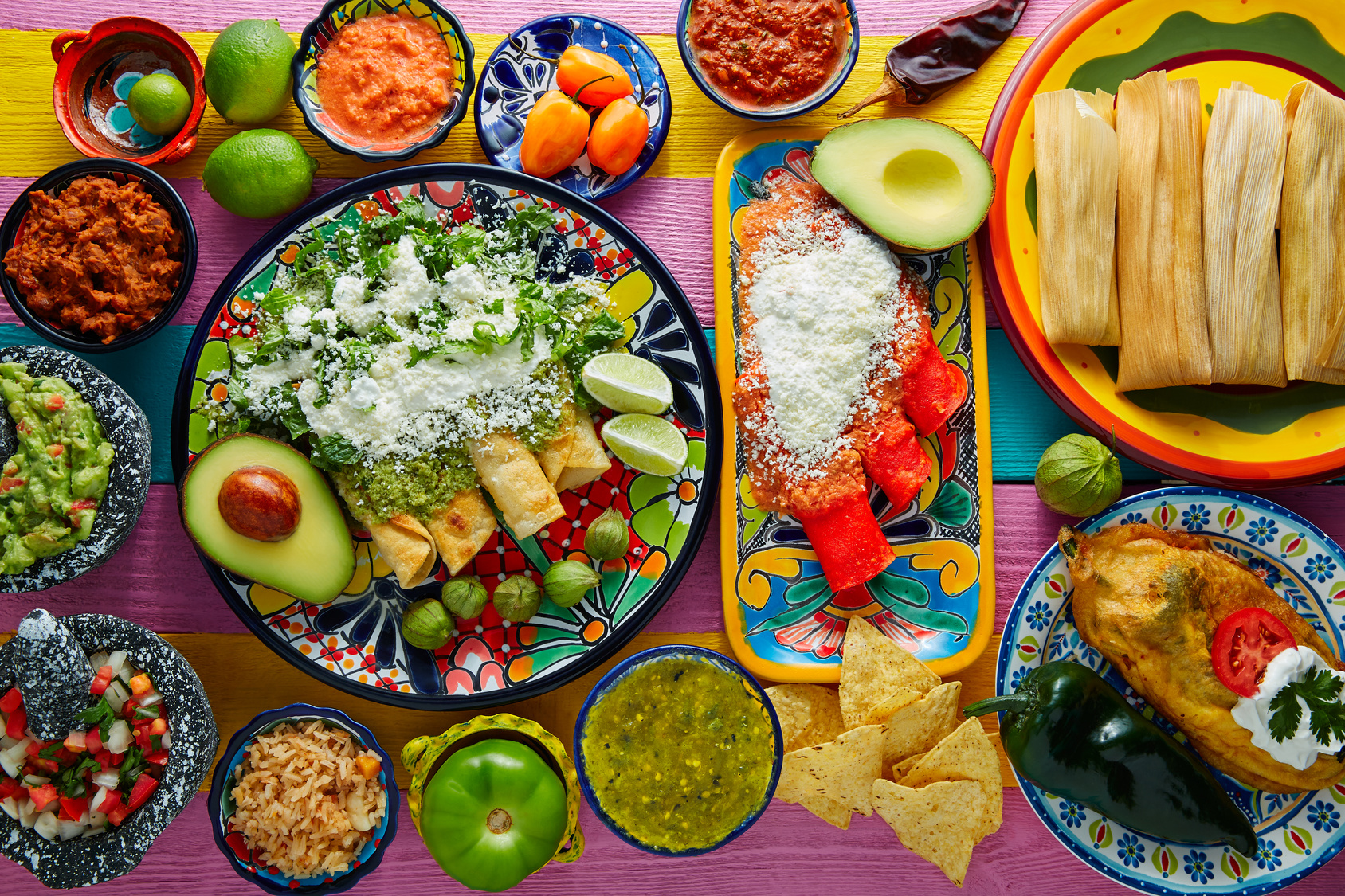 Green and red enchiladas with mexican sauces mix in colorful table
