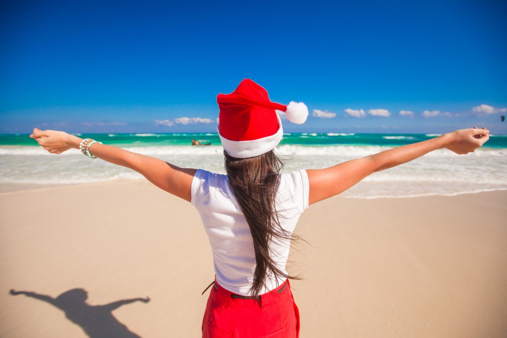 Back view of beautiful girl in Santa Hat walking spread her hands on white beach