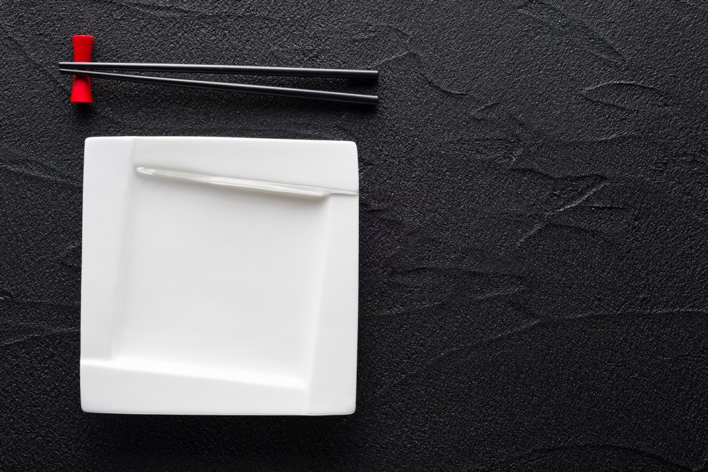 Chopsticks and white plate on black rock